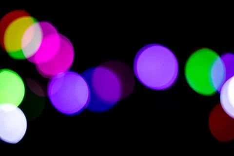 Multicolored bokeh circles form a soft wavy wave line against dark background Stock Photos