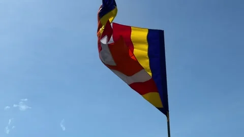 A multicolored Buddhist flag waves freely in the wind against a clear blue sky 库存影片 329745664