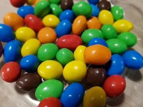 Multicolored chocolate-covered nuts in a transparent plate Stock Photos