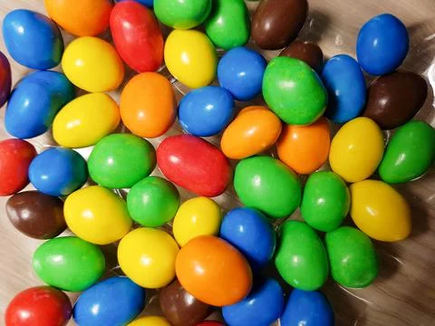 Multicolored chocolate-covered nuts in a transparent plate Stock Photos
