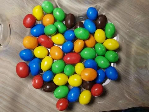 Multicolored chocolate-covered nuts in a transparent plate Stock Photos