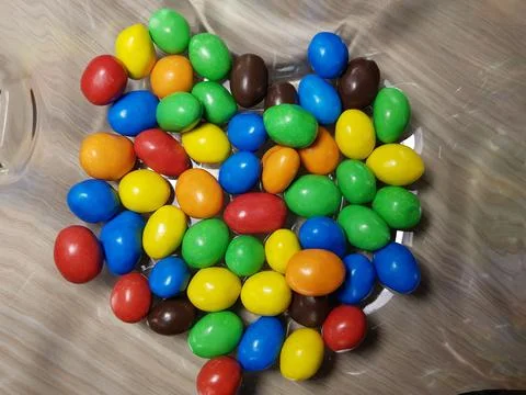 Multicolored chocolate-covered nuts in a transparent plate Stock Photos