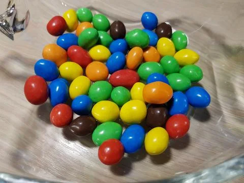 Multicolored chocolate-covered nuts in a transparent plate Stock Photos