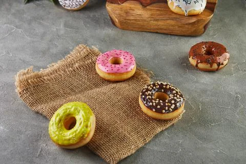 Multicolored donuts with glaze and splashes with flowers on a gray background Stock Photos