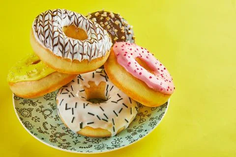 Multicolored donuts with icing and splashes on a blue plate on a yellow backg Stock Photos