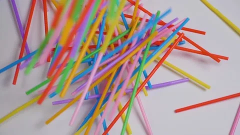 Multicolored drinking straws falling on white table. Slow motion. Stock Footage 132490512