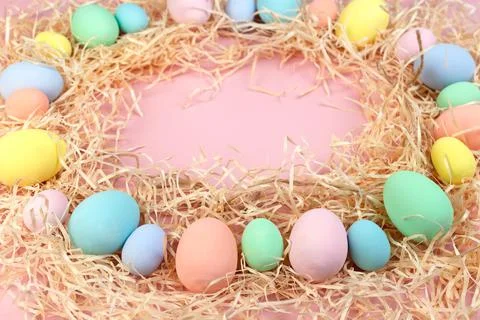 Multicolored Easter eggs and feathers in pastel colors lie on shavings in the Stock Photos