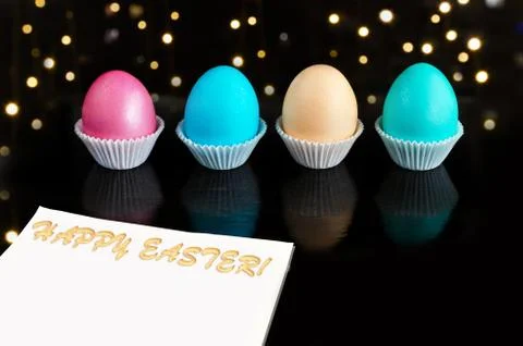 Multicolored Easter eggs on a black background with bokeh. A piece of paper w Photos