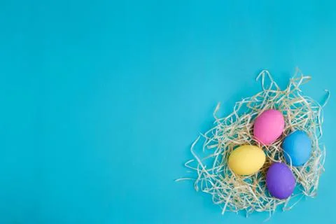 Multicolored Easter eggs in hay, flat lay with copy space Stock Photos