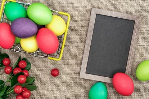 Multicolored Easter eggs in a metal basket and a frame with a chalk board. Stock Photos