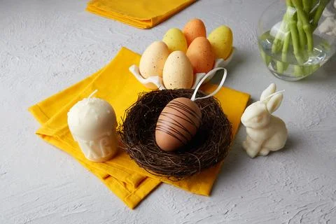Multicolored Easter eggs in a nest and on a tray next to white candles Stock Photos