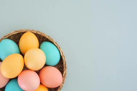 Multicolored easter eggs in pastel shades in a basket on a blue background with Stock Photos