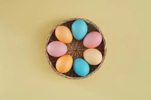 Multicolored Easter eggs in pink, yellow and blue tones in a basket on a pastel Stock Photos