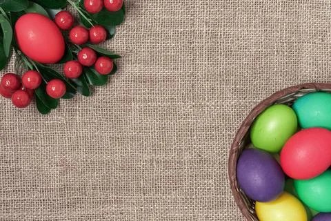 Multicolored Easter eggs in a wicker basket and red berries on burlap background Stock Photos
