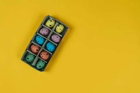 Multicolored Easter quail eggs in carton box isolated on yellow background Stock Photos