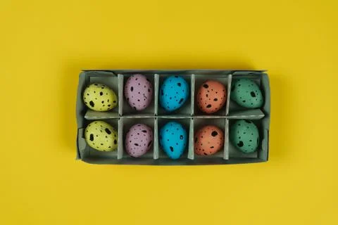 Multicolored Easter quail eggs in carton box isolated on yellow background Stock Photos