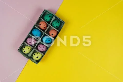 Multicolored Easter quail eggs in carton box isolated on pink and yellow Stock Photos