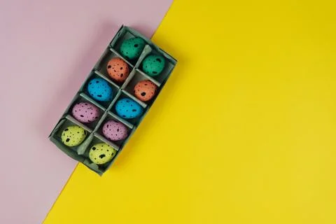 Multicolored Easter quail eggs in carton box isolated on pink and yellow Stock Photos