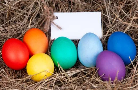 Multicolored eggs with a note in the a hay. Mock up, concept easter. Stock Photos