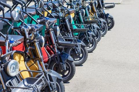 Multicolored electric bikes with headlights and baskets stand in a row on a Stock Photos