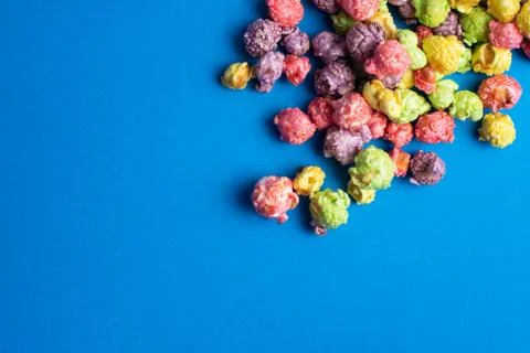Multicolored fruit flavored popcorn on blue background. Candy coated popcorn. Stock Photos