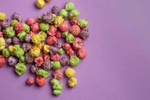 Multicolored fruit flavored popcorn on pink background. Candy coated popcorn. Stock Photos