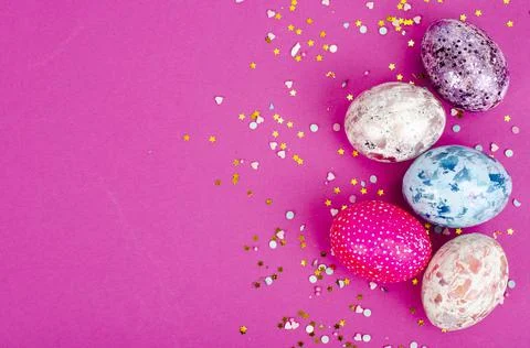 Multicolored handmade easter eggs and confetti on pink background. Minimal co Stock Photos