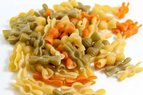 Multicolored macaroni close-ups fall from above on a white background. Stock Photos