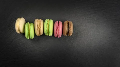 Multicolored macarons in a row on a black background with copy space Foto stock