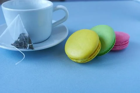 Multicolored macaroons and tea bag with mug on blue background. Stock Photos