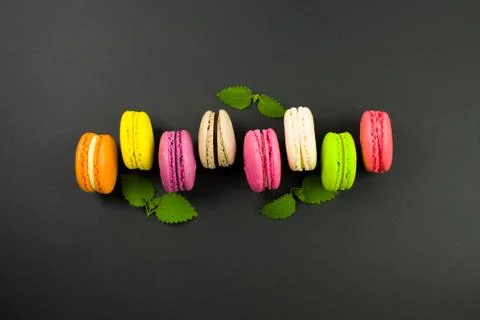 Multicolored macaroons on a black background, top view. Mint leaves 스톡 사진