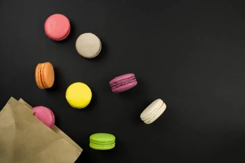 Multicolored macaroons on a black background, top view. paper bag Stock-Fotos