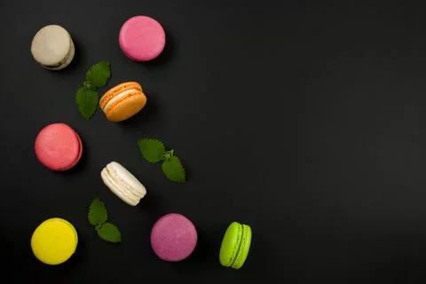 Multicolored macaroons on a black background, top view. Mint leaves 스톡 사진