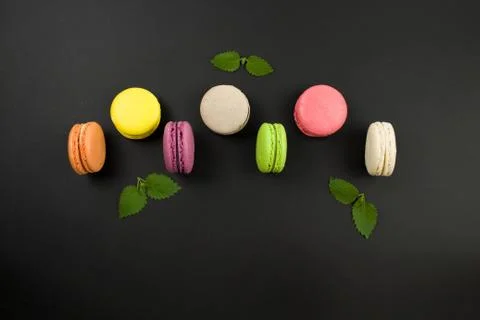 Multicolored macaroons on a black background, top view. Mint leaves 스톡 사진