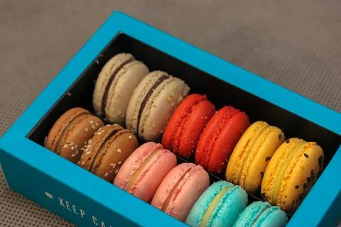 Multicolored macaroons in blue box on gray background, French dessert flat lay Stock Photos