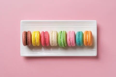 Multicolored macaroons on a rectangular plate against pastel pink background. Stock Photos