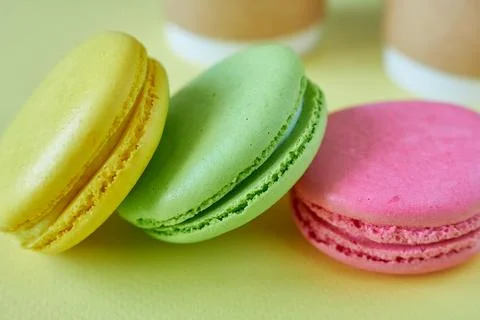Multicolored macaroons on a yellow background with coffee in cups. Stock Photos
