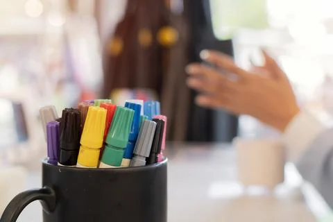 Multicolored marker pens in a black ceramic mug with blurred image of woman.. Stock Photos
