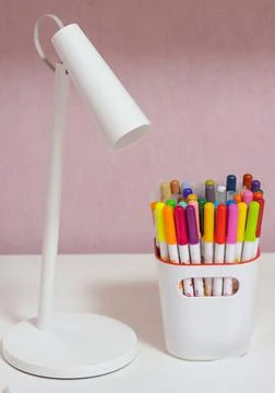 Multicolored markers in a white container and white table lamp Stock Photos