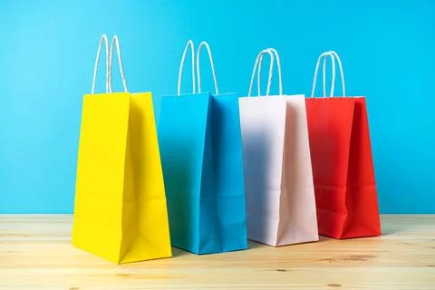 Multicolored packages of paper on a colored background and a wooden table. Stock Photos