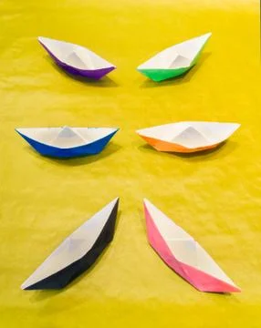 Multicolored paper boats on yellow surface symmetrically arranged Stock Photos