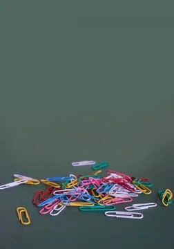 Multicolored paper clips lie on a plain green background. Vertical format Stock Photos