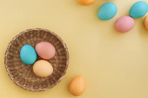 Multicolored pastel easter eggs in a basket and on a yellow background with Stock Photos