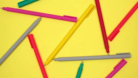 Multicolored pens randomly lie on rotating yellow background stationery supplies Stock Footage 231451761