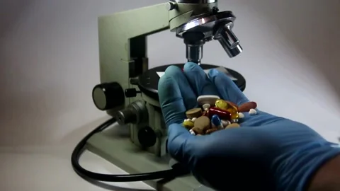 Multicolored pills pour into a doctor's gloved hand against the microscope Stock Footage 317296913