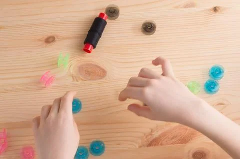 Multicolored plastic bobbin for sewing machine. and kid's hands in .wooden ba Stock Photos