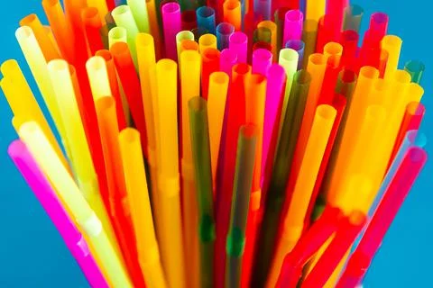 Multicolored plastic drinking cocktail straws, close up, blue background. Mak Stock Photos