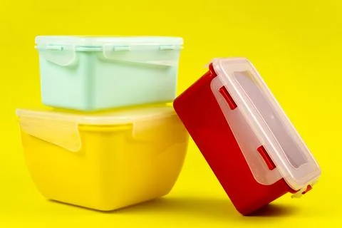 Multicolored plastic lunch boxes on yellow background, side view. Stock Photos