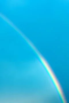 Multicolored rainbow on the background of the blue sky. Vertical photo Stock Photos