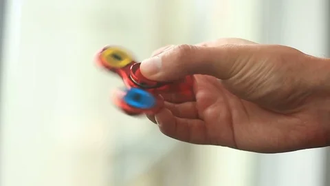 Multicolored, red-yellow-blue hand spinner, or fidgeting spinner, rotating on Stock Footage 76908314